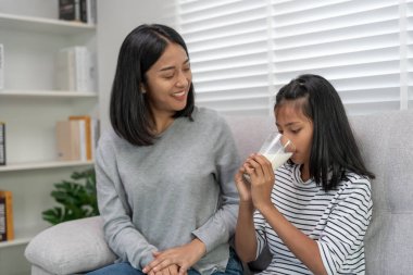 Asyalı küçük kız evde öğreniyor. Nazik anneyle ödev yap, sınav için cesaretlendir. Anne, kızına bir bardak süt ver. Kız mutlu bir ev okulu. Annem birlikte eğitim veriyor..