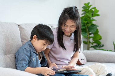 Küçük çocukla tablet kullanarak öğretmencilik oynayan mutlu bekar anne. Aile evde mutlu ve heyecanlı. Anne ve oğul birlikte vakit geçiriyorlar, iyi baba, bağımlılık düzelt, kontrol et, kontrol et.