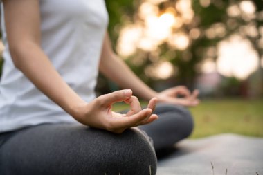 Kadın parkta meditasyon yapıyor. Sabahları egzersiz yapan Asyalı bir kadın. denge, dinlenme, rahatlama, sakinlik, sağlık, mutluluk, rahatlama, sağlıklı yaşam tarzı, stresi azaltma, huzur, tutum.
