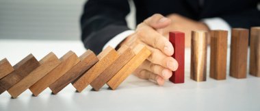 Domino 'yu elleri olan sigorta korur. İş adamı elleri iş krizinde domino taşlarının düşmesini durdurur. işletme risk denetimi ve planlama ve işletmeler sigorta işletmelerini önlemek için stratejiler.