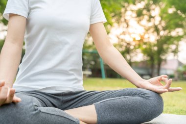 Kadın parkta meditasyon yapıyor. Sabahları egzersiz yapan Asyalı bir kadın. denge, dinlenme, rahatlama, sakinlik, sağlık, mutluluk, rahatlama, sağlıklı yaşam tarzı, stresi azaltma, huzur, tutum