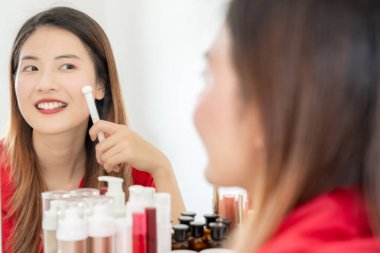 Güzel bir Asyalı kadın aynanın karşısına oturur ve makyaja gülümser. Makyaj yapan sağlıklı bir kadının yüzü. Reklam, yaşam tarzı, kozmetik, makyaj malzemeleri, güzellik etkinliği, güzellik uzmanı.