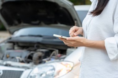 breakdown, broken car, repair. Woman uses mobile phone check insurance premiums through application due to car accident . Find garage to get car fixed during country tour, waiting for help, emergency