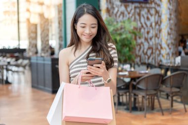 Modern happy asian Female lifestyle fashion portrait. beautiful attractive young woman girl enjoy stylish walk with shopping bag packages use smartphone on the street, trendy outfit on shopping mall