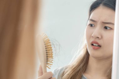 Asyalı kadın çok üzgün ve üzgün. Hasarlı saçlara, saç dökülmesine, saç dökülmesine, vitamin eksikliğine, kelliğe, doğum sonrası depresyona, çinko, regl veya endokrin bozukluklarına, hormonal dengesizliğe bakıyor.
