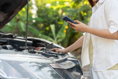 breakdown, broken car, repair. Woman uses mobile phone check insurance premiums through application due to car accident . Find garage to get car fixed during country tour, waiting for help, emergency