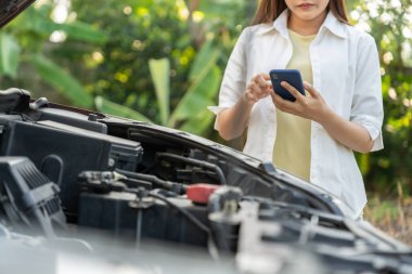 breakdown, broken car, repair. Woman uses mobile phone check insurance premiums through application due to car accident . Find garage to get car fixed during country tour, waiting for help, emergency.