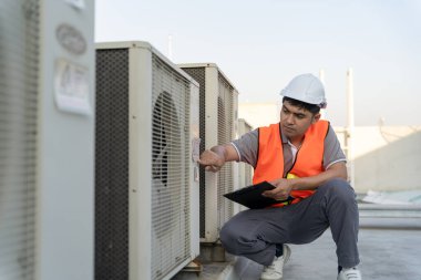 Asyalı bakım mühendisi fabrikanın çatısında çalışıyor. Müteahhit kompresör sistemini denetleyecek ve inşaatta havalandırma sistemi kurmayı planlıyor. Kontrol listesi, müfettiş, kontro