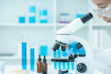 Bilimadamı ileri bilimsel laboratuvarda biyokimyasal örnekleri analiz ediyor. Tıbbi profesyonel kullanım mikroskobu virüsün mikrobiyolojik gelişimini gösteriyor. Fen laboratuvarında biyoteknoloji araştırması.