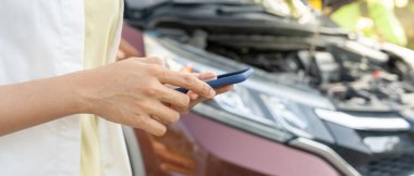 breakdown, broken car, repair. Woman uses mobile phone check insurance premiums through application due to car accident . Find garage to get car fixed during country tour, waiting for help, emergency.