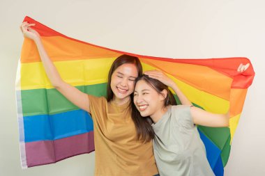 LGBT grubu. Güzel görünümlü lezbiyen çiftler gökkuşağı bayraklarını parlak bir şekilde örterler. Asyalı genç çift birbirlerine mutlu bir şekilde sarılıyorlar, aşık olan sevgili, biseksüeller, homoseksüellik, özgürlük, ifade, mutlu hayat.