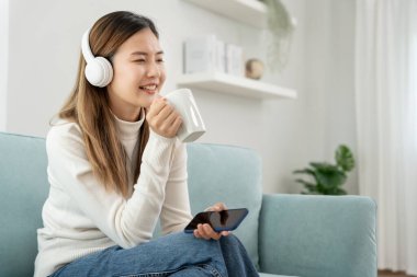 Kablosuz kulaklıklı neşeli genç Asyalı kadınlar oturup müzik dinliyor, eğleniyor, müzik dinliyor, kolunu kaldırıyor, en sevdiği şarkıyla dans ediyor, harika bir soundtrack 'in keyfini çıkarıyor, mutlu bir hayat sürüyor, eğleniyor.