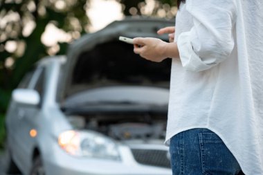 breakdown, broken car, repair. Woman uses mobile phone check insurance premiums through application due to car accident . Find garage to get car fixed during country tour, waiting for help, emergency.