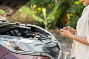 breakdown, broken car, repair. Woman uses mobile phone check insurance premiums through application due to car accident . Find garage to get car fixed during country tour, waiting for help, emergency.