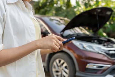 breakdown, broken car, repair. Woman uses mobile phone check insurance premiums through application due to car accident . Find garage to get car fixed during country tour, waiting for help, emergency.