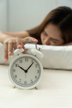 Tembel Asya 'lı genç kadın saat alarmını kapatıyor, bayan geç kalıyor ya da işe gidiyor ya da ders çalışıyor, uyuyakalıyor, sabahları uyanıyor, endişeleniyor, uykulu, geç kalmış, acele et.