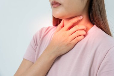 Asyalı kadın boğazı ağrıdığı için elini boynuna koydu. Dişi bademcik iltihabı iltihaba neden olur. Su alarak, antibiyotik alarak, doktora, virüse, korona virüsüne, gribe, gribe danışarak tedavi olunur.