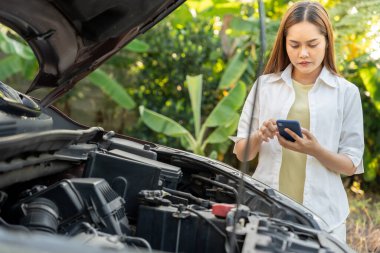 breakdown, broken car, repair. Woman uses mobile phone check insurance premiums through application due to car accident . Find garage to get car fixed during country tour, waiting for help, emergency.