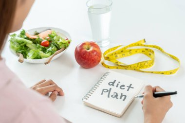 Kadınlar diyet için sağlıklı yiyecekleri seçerler. Sağlıklı yiyecekler ve yağlı yiyecekler mezurayla ayrılmış. Kilo ver, denge ver, kontrol et, yağ düşür, düşük kalori, rutin egzersiz, vücut şekli.