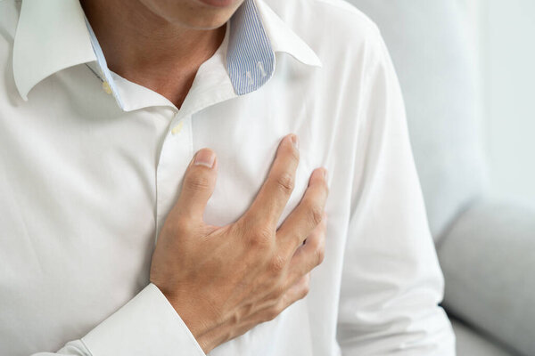 рука держать грудь с симптомами сердечного приступа, азиатский человек упорно работают есть боли в груди, вызванные болезнью сердца, утечка, расширение, увеличенное коронарное сердце, нажмите на грудь с болезненным выражением