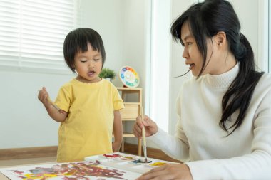 Mutlu Asyalı anne küçük kız için boya öğreniyor. Komik aile evde mutlu ve heyecanlı. Anne ve kızı birlikte vakit geçiriyorlar. Tatil, etkinleştir