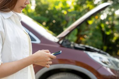 breakdown, broken car, repair. Woman uses mobile phone check insurance premiums through application due to car accident . Find garage to get car fixed during country tour, waiting for help, emergency.