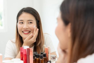 Güzel bir kadın aynanın önünde oturur. Krem sürerek makyaj yapan sağlıklı bir kadın yüzü. Cilt kremi reklamı, kırışıklık önleyici, bebek yüzü, beyazlatma, nemlendirici, gözenekleri sıkma seru