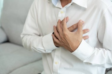 Kalp krizi belirtileriyle el ele tutuşan Asyalı adamın göğüs ağrısı var. Kalp rahatsızlığı, sızıntı, genişleme, genişlemiş kalp, göğsüne acı veren bir ekspresyoyla bastırma.