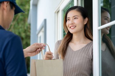 Mutlu gülümseyen Asyalı kadın, kurye evinden bir paket yiyecek alıyor. Teslimatçı ekspres teslimat gönderdi. Çevrimiçi alışveriş, kağıt konteynır, paket servisi, postacı, dağıtım servisi, paketler