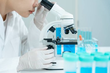 Bilimadamı ileri bilimsel laboratuvarda biyokimyasal örnekleri analiz ediyor. Tıbbi profesyonel kullanım mikroskobu virüsün mikrobiyolojik gelişimini gösteriyor. Fen laboratuvarında biyoteknoloji araştırması.