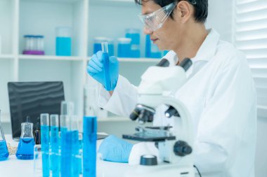 Bilimadamı ileri bilimsel laboratuvarda biyokimyasal örnekleri analiz ediyor. Tıbbi profesyonel kullanım mikroskobu virüsün mikrobiyolojik gelişimini gösteriyor. Fen laboratuvarında biyoteknoloji araştırması.