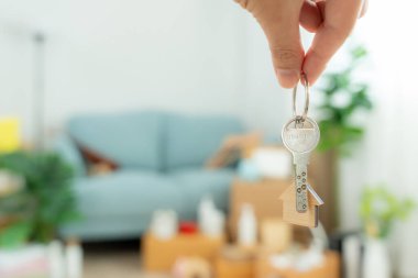 Moving house, relocation. Man hold key house keychain in new apartment, inside the room was a cardboard box containing personal belongings and furniture. move in the apartment or condominium