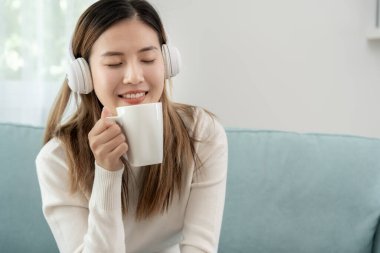 Kablosuz kulaklıklı neşeli genç Asyalı kadınlar oturup müzik dinliyor, eğleniyor, müzik dinliyor, kolunu kaldırıyor, en sevdiği şarkıyla dans ediyor, harika bir soundtrack 'in keyfini çıkarıyor, mutlu bir hayat sürüyor, eğleniyor.
