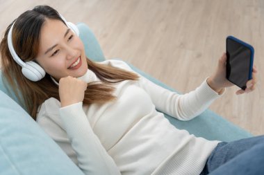 Kablosuz kulaklıklı neşeli genç Asyalı kadınlar oturup müzik dinliyor, eğleniyor, müzik dinliyor, kolunu kaldırıyor, en sevdiği şarkıyla dans ediyor, harika bir soundtrack 'in keyfini çıkarıyor, mutlu bir hayat sürüyor, eğleniyor.
