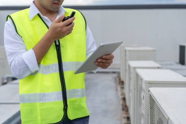 Asyalı bakım mühendisi fabrikanın çatısında çalışıyor. Müteahhit kompresör sistemini denetleyecek ve inşaatta havalandırma sistemi kurmayı planlıyor. teknoloji, çevrimiçi, mobil uygulama.