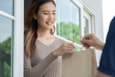 Mutlu gülümseyen Asyalı kadın, kurye evinden bir paket yiyecek alıyor. Teslimatçı ekspres teslimat gönderdi. Çevrimiçi alışveriş, kağıt konteynır, paket servisi, postacı, dağıtım servisi, paketler