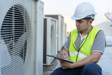 Asyalı bakım mühendisi fabrikanın çatısında çalışıyor. Müteahhit kompresör sistemini denetleyecek ve inşaatta havalandırma sistemi kurmayı planlıyor. Kontrol listesi, müfettiş, kontro