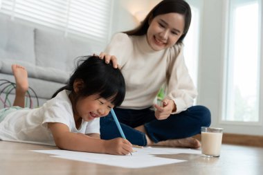 Anne kızına resim öğretiyor. Asyalı küçük kız öğrenip oynuyor. Nazik anneyle ödev yap, sınav için cesaretlendir. Kız mutlu bir ev okulu. Annelik eğitimi..