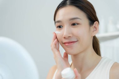 Güzel bir kadın aynanın önünde oturur. Krem sürerek makyaj yapan sağlıklı bir kadın yüzü. Cilt kremi reklamı, kırışıklık önleyici, bebek yüzü, beyazlatma, nemlendirici, gözenekleri sıkılaştırma serumu.