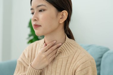 Asyalı kadın boğazı ağrıdığı için boynuna takıldı. Dişi bademcik iltihabı iltihaba neden olur. Su alarak, antibiyotik alarak, doktora, virüse, korona virüsüne, grip virüsüne danışarak,