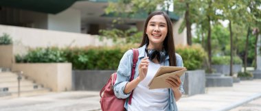 Sırt çantası ve kitapları açık havada olan Asyalı güzel bir öğrenci. Üniversite kampüsünde kitap taşımaktan mutlu gülümseyen kız. Uluslararası Asya Üniversitesi 'nde kadın portresi. Eğitim, eğitim, okul