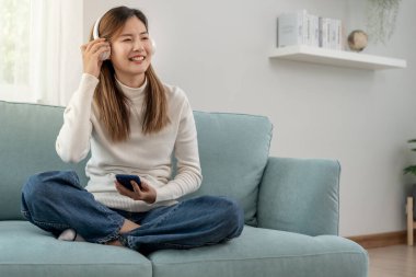 Kablosuz kulaklıklı neşeli genç Asyalı kadınlar oturup müzik dinliyor, eğleniyor, müzik dinliyor, kolunu kaldırıyor, en sevdiği şarkıyla dans ediyor, harika bir soundtrack 'in keyfini çıkarıyor, mutlu bir hayat sürüyor, eğleniyor.