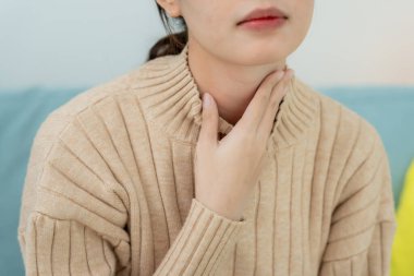 Asyalı kadın boğazı ağrıdığı için boynuna takıldı. Dişi bademcik iltihabı iltihaba neden olur. Su alarak, antibiyotik alarak, doktora, virüse, korona virüsüne, grip virüsüne danışarak,