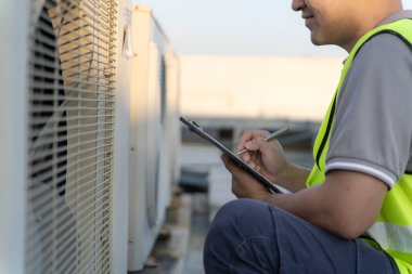 Bakım mühendisi fabrikanın çatısında çalışıyor. Müteahhit kompresör sistemini denetleyecek ve inşaatta havalandırma sistemi kurmayı planlıyor. Kontrol listesi, müfettiş, kontrol