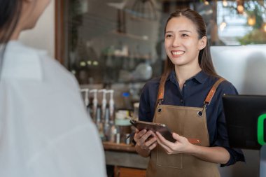 Asya 'lı kadın mutlu ve gülümseyen müşteri siparişi alıyor. Güvenliği, temizliği ve kafeyi açmayı garanti ediyor. Yeni normallere açık. Küçük işletme, hoş geldin, restoran, ev yapımı, kafe.