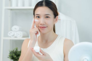 Güzel Asyalı kadın gülümsüyor, cilt kremi kullanıyor. Sağlıklı bir kadın yüzüne krem sürün ve makyaj yapın. Cilt kremi reklamı, kırışıklık önleyici, bebek yüzü, beyazlatma, nemlendirici, gözenekleri sıkma seru