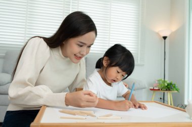 Mutlu Asyalı anne küçük kız için boya öğreniyor. Aile evde mutlu ve heyecanlı. Anne ve kızı birlikte vakit geçiriyorlar. Tatil, Faaliyet, Yönetici Fonksiyonu, IQ, EQ