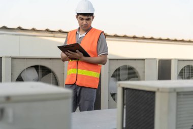 Asyalı bakım mühendisi fabrikanın çatısında çalışıyor. Müteahhit kompresör sistemini denetleyecek ve inşaatta havalandırma sistemi kurmayı planlıyor. Kontrol listesi, müfettiş, kontrol