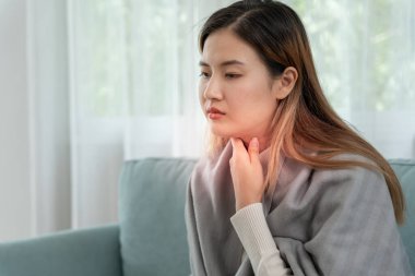 Asyalı kadın boğazı ağrıdığı için boynuna takıldı. Dişi bademcik iltihabı iltihaba neden olur. Su alarak, antibiyotik alarak, doktora, virüse, korona virüsüne, grip virüsüne danışarak,