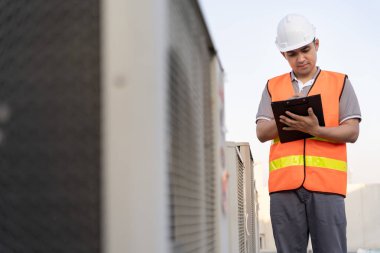 Asyalı bakım mühendisi fabrikanın çatısında çalışıyor. Müteahhit kompresör sistemini denetleyecek ve inşaatta havalandırma sistemi kurmayı planlıyor. Kontrol listesi, müfettiş, kontro